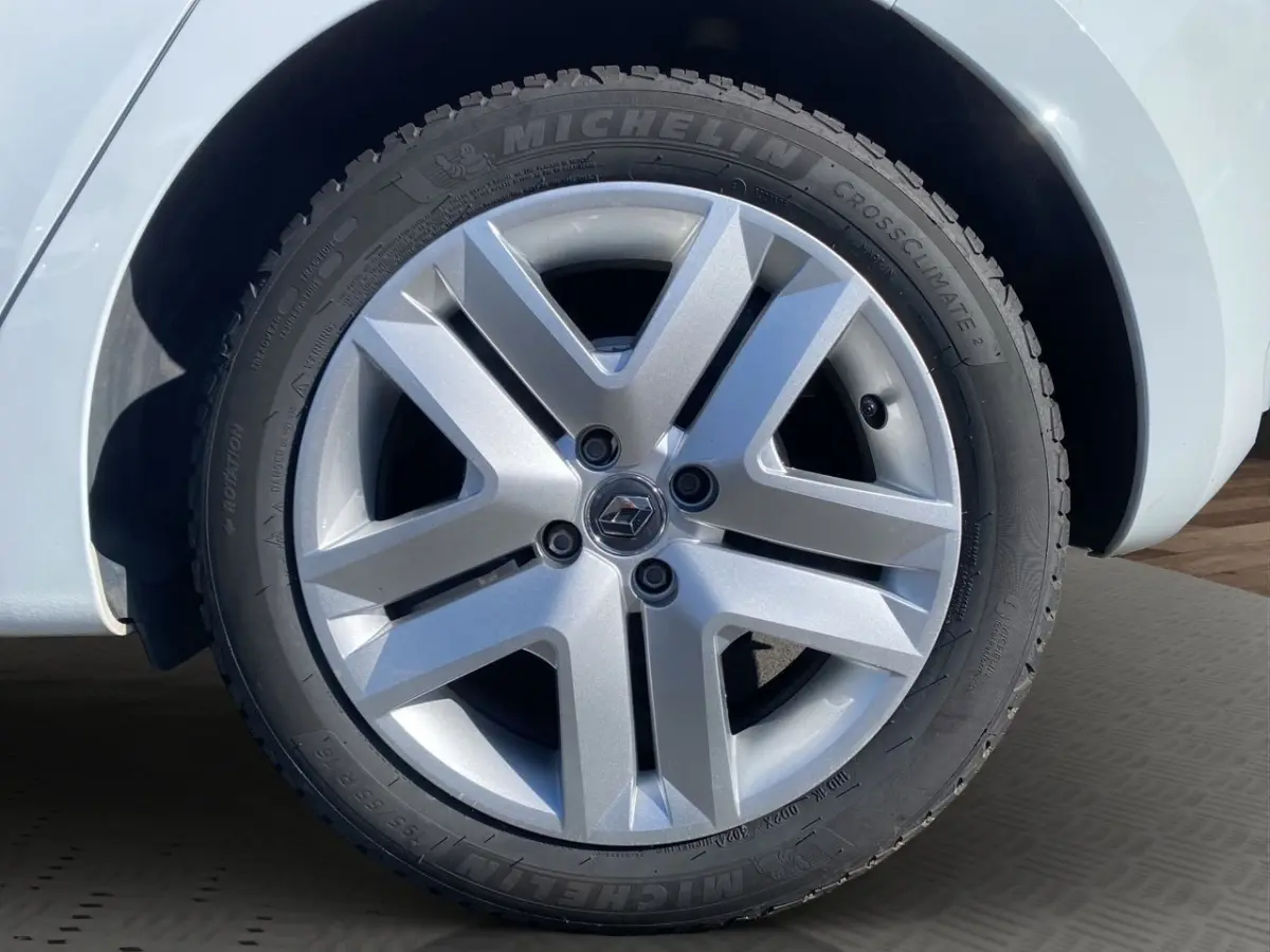 Gros plan sur la roue avant gauche d'une Renault Clio blanche avec jante alliage et pneu Michelin CrossClimate.