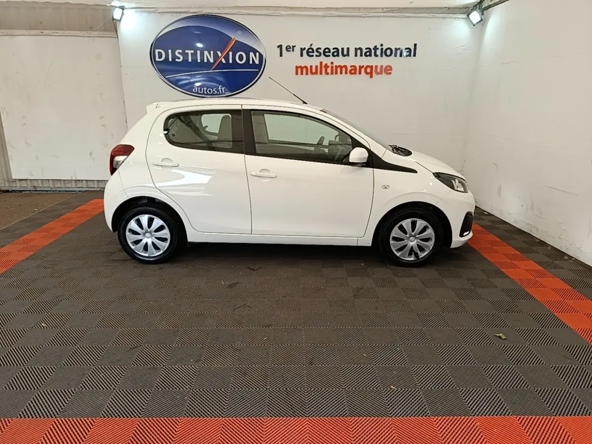 Profil droit d'une Peugeot 108 blanche VTI 72 S&S Active, compacte et citadine, dans un showroom intérieur.