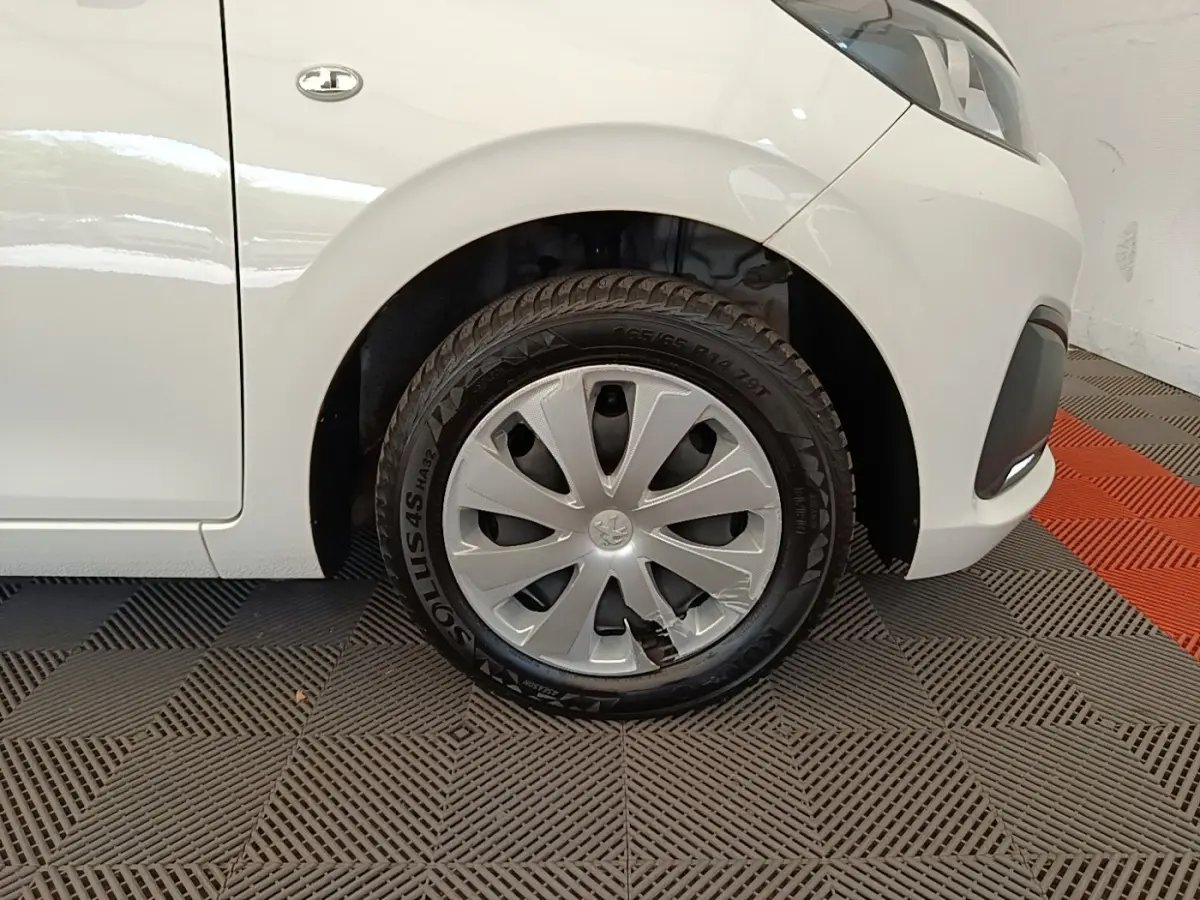 Gros plan sur la roue avant gauche d'une Peugeot 108 blanche, avec enjoliveur abîmé visible sur le pneu.