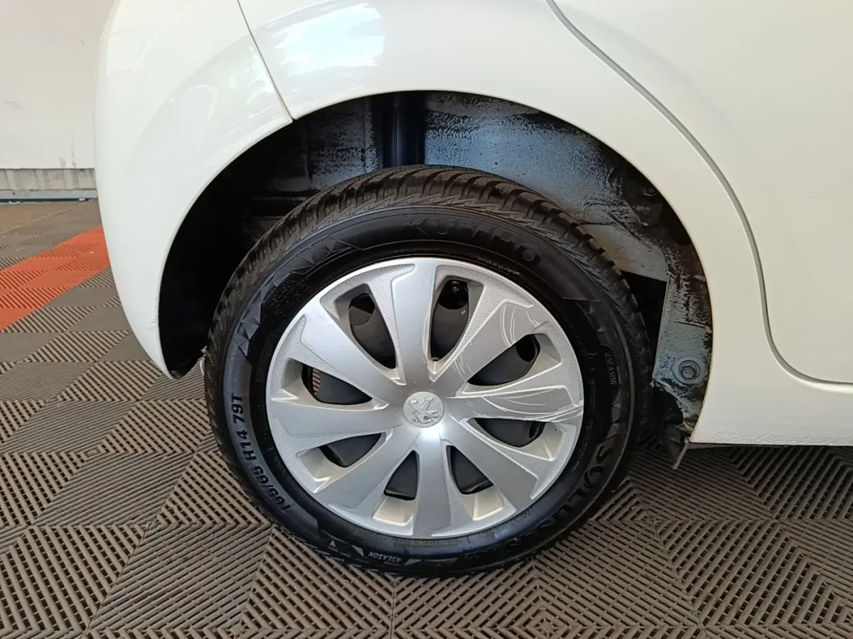 Gros plan sur la roue arrière droite d'une Peugeot 108 blanche, avec enjoliveur argenté et pneu noir visible.