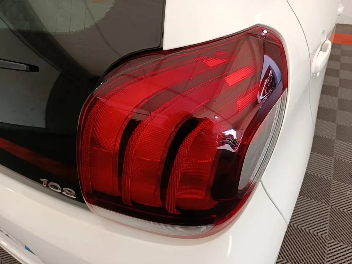 Gros plan sur le feu arrière droit rouge d’une Peugeot 108 blanche, avec une partie de la lunette arrière visible.