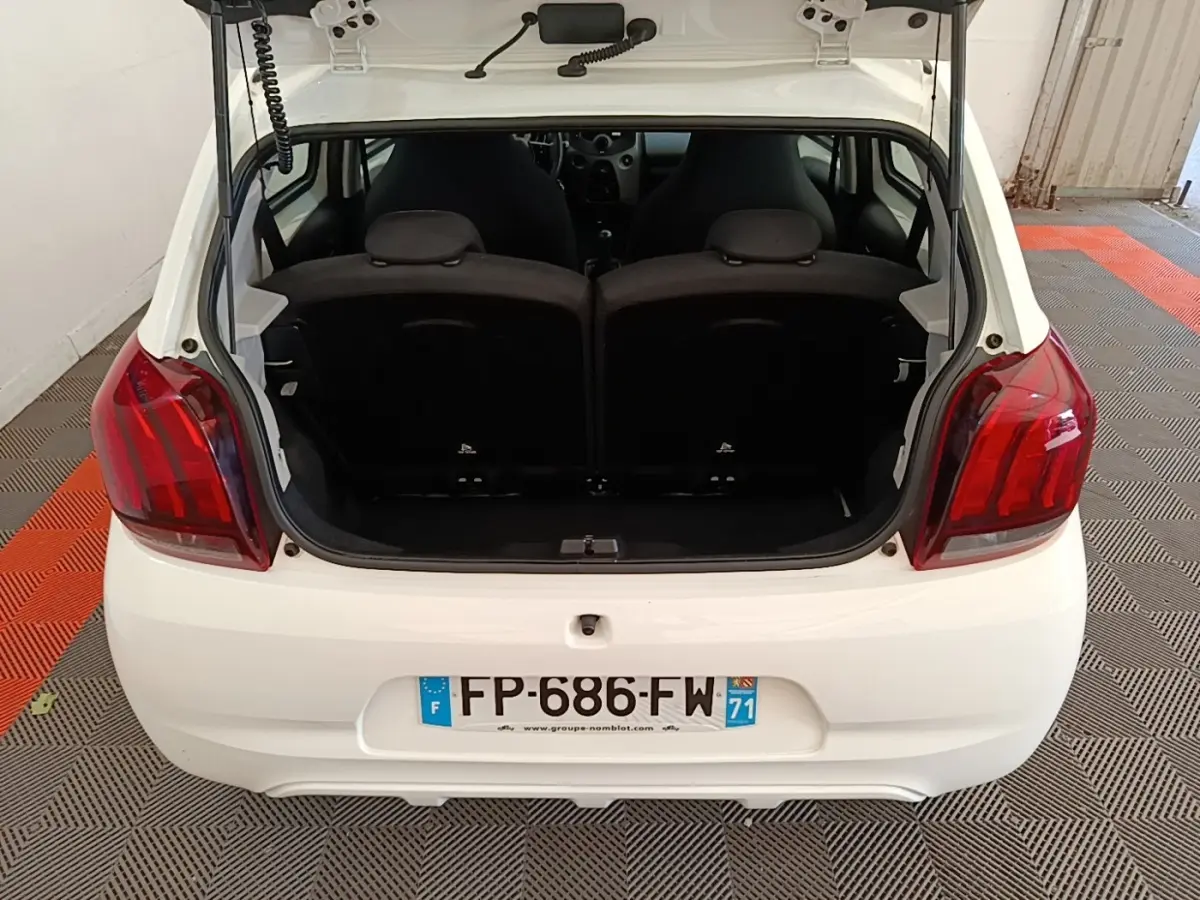 Vue arrière d'une Peugeot 108 blanche avec coffre ouvert, montrant les sièges arrière et les feux rouges.