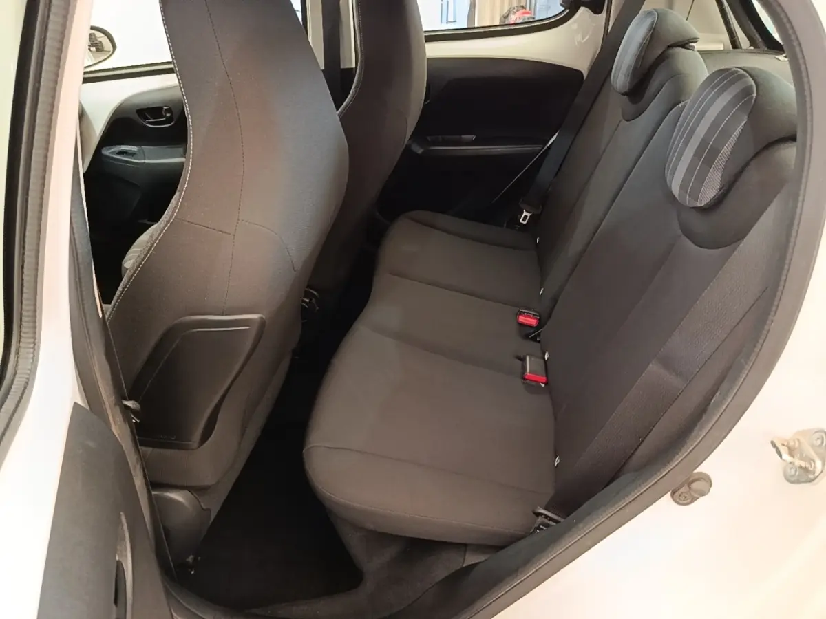 Vue intérieure côté droit sur la banquette arrière noire d'une Peugeot 108 blanche, avec appuie-têtes et ceintures visibles.