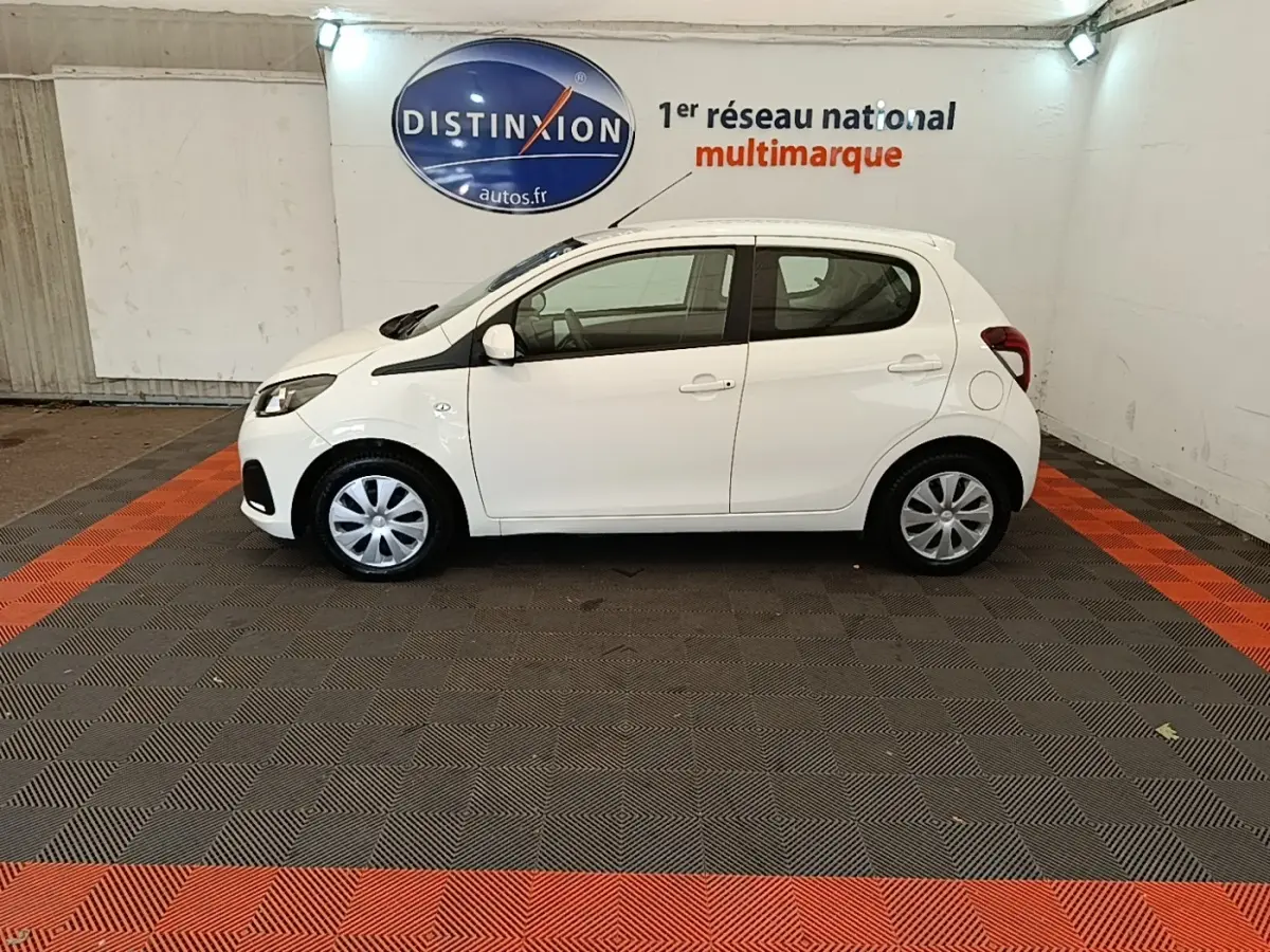 Profil droit d'une Peugeot 108 blanche VTI 72 S&S Active, compacte et citadine, dans un showroom intérieur.