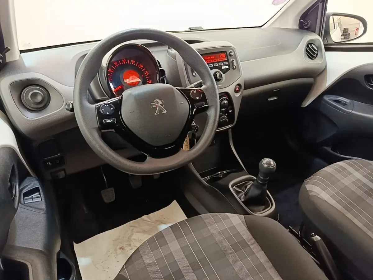Intérieur de Peugeot 108 blanc, vue côté conducteur sur le volant multifonctions et la console centrale avec boîte manuelle.