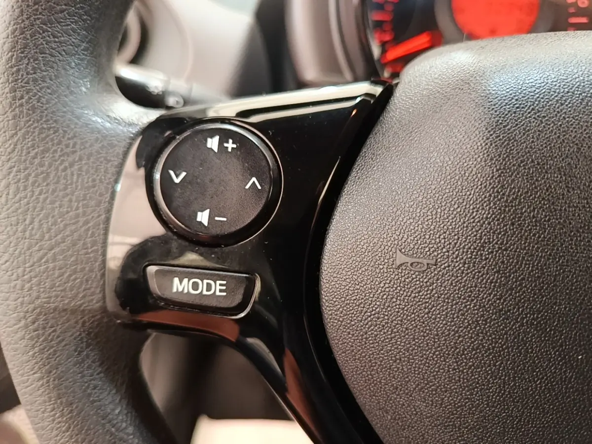 Gros plan sur le volant multifonctions noir de la Peugeot 108 blanc, avec commandes de volume et bouton mode visibles.