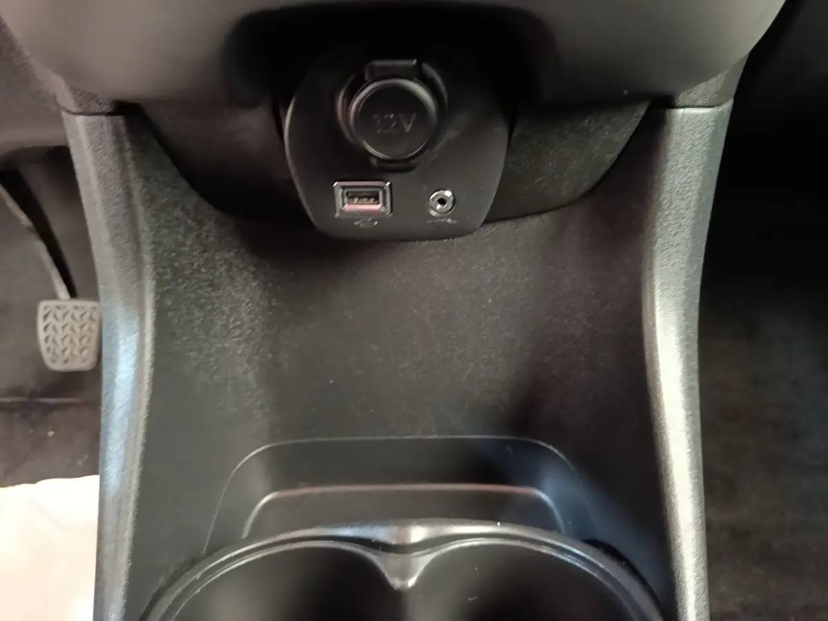 Vue rapprochée de la console centrale noire du Peugeot 108 avec prise 12V, port USB et prise jack.
