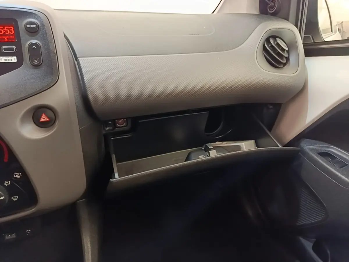Vue intérieure côté passager du tableau de bord gris clair et boîte à gants ouverte d'une Peugeot 108 blanche de 2020.