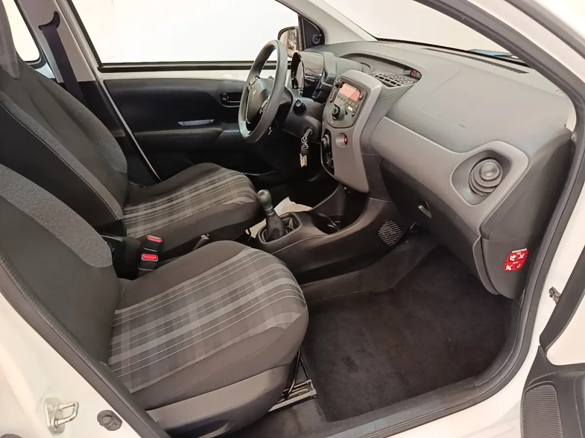 Vue intérieure côté conducteur de la Peugeot 108 blanche, montrant sièges à motifs et tableau de bord compact.