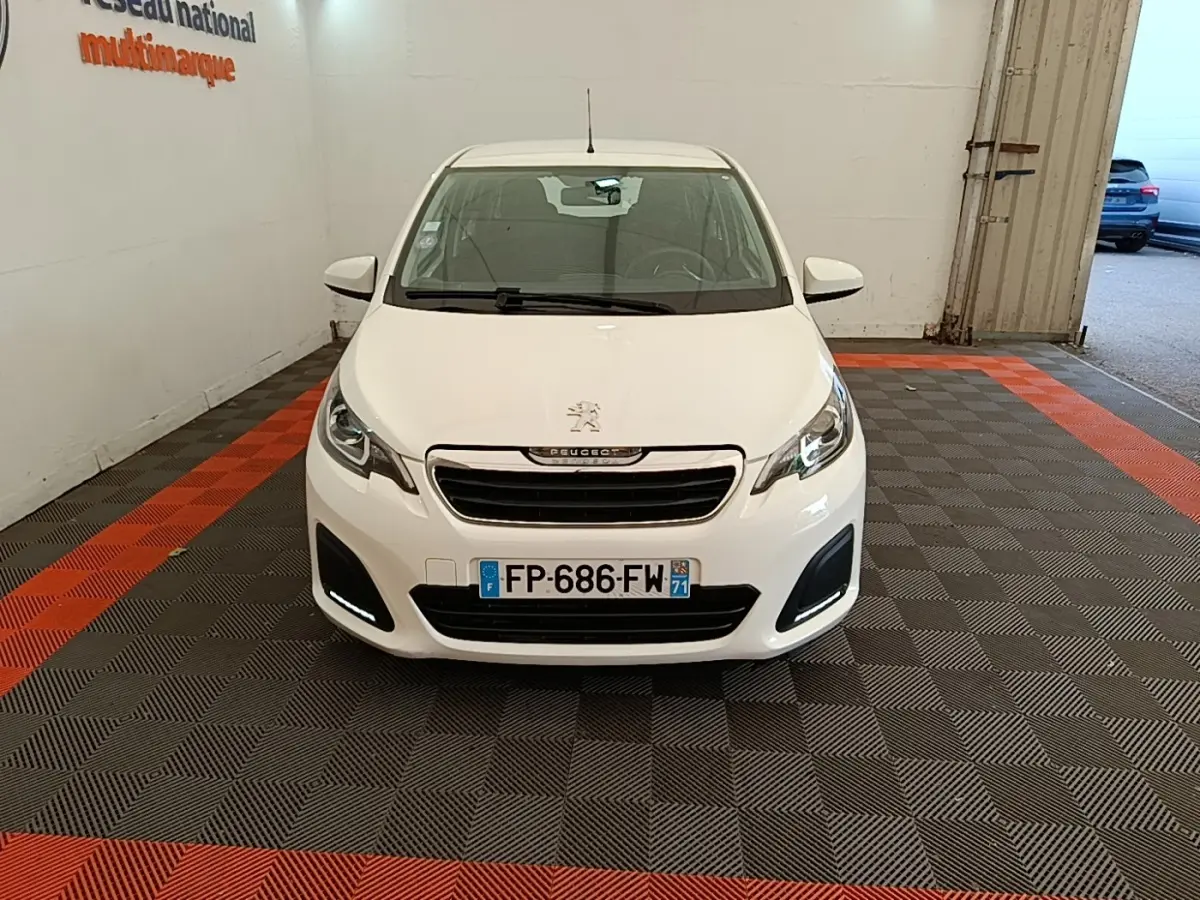 Peugeot 108 blanc vue de face dans un garage avec feux diurnes LED allumés et plaque d'immatriculation visible.