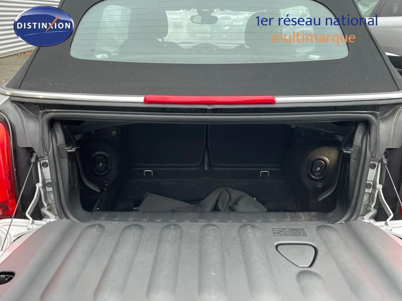 Coffre ouvert vu de l'arrière d'une MINI Cabriolet F57 2023 couleur Melting Silver Metal avec toit noir relevé.