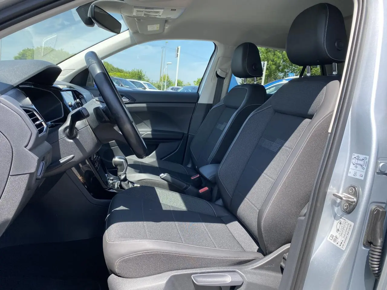 Vue intérieure côté conducteur du Volkswagen T-Cross 2022 argent, montrant sièges avant en tissu gris et tableau de bord moderne.