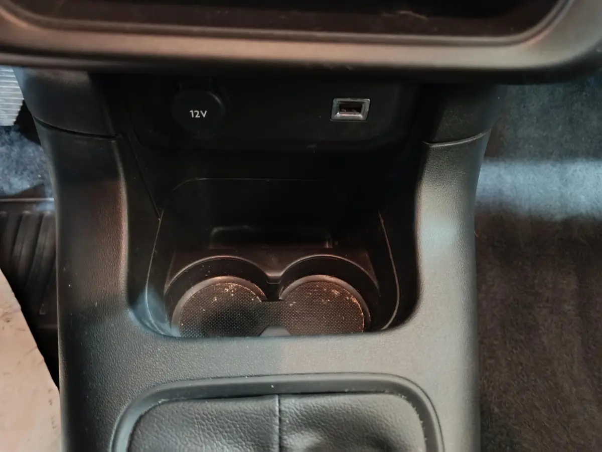 Gros plan sur la console centrale noire de la Citroën C3 2024 avec prise 12V, port USB et porte-gobelets.