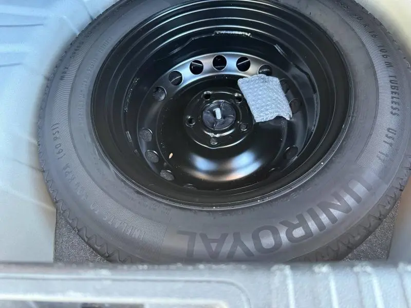Roue de secours noire en acier avec pneu Uniroyal, logée dans le coffre d'un Renault Captur blanc nacré 2025.