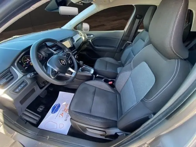 Vue intérieure côté conducteur du Renault Captur gris clair 2023, volant multifonctions en cuir synthétique et tableau de bord digital.