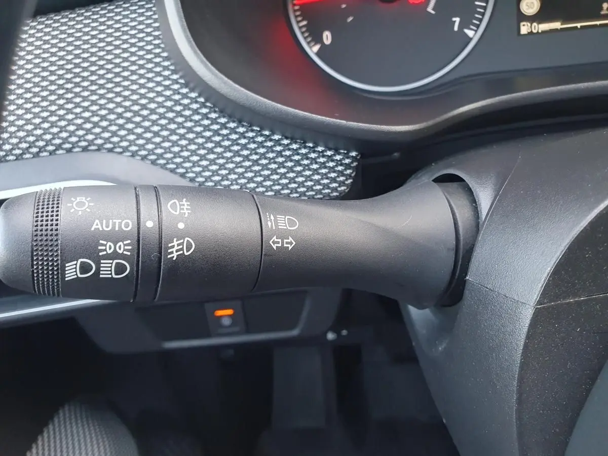 Gros plan sur la commande des feux et clignotants côté gauche du volant dans un intérieur gris d'une Dacia Sandero 2024.