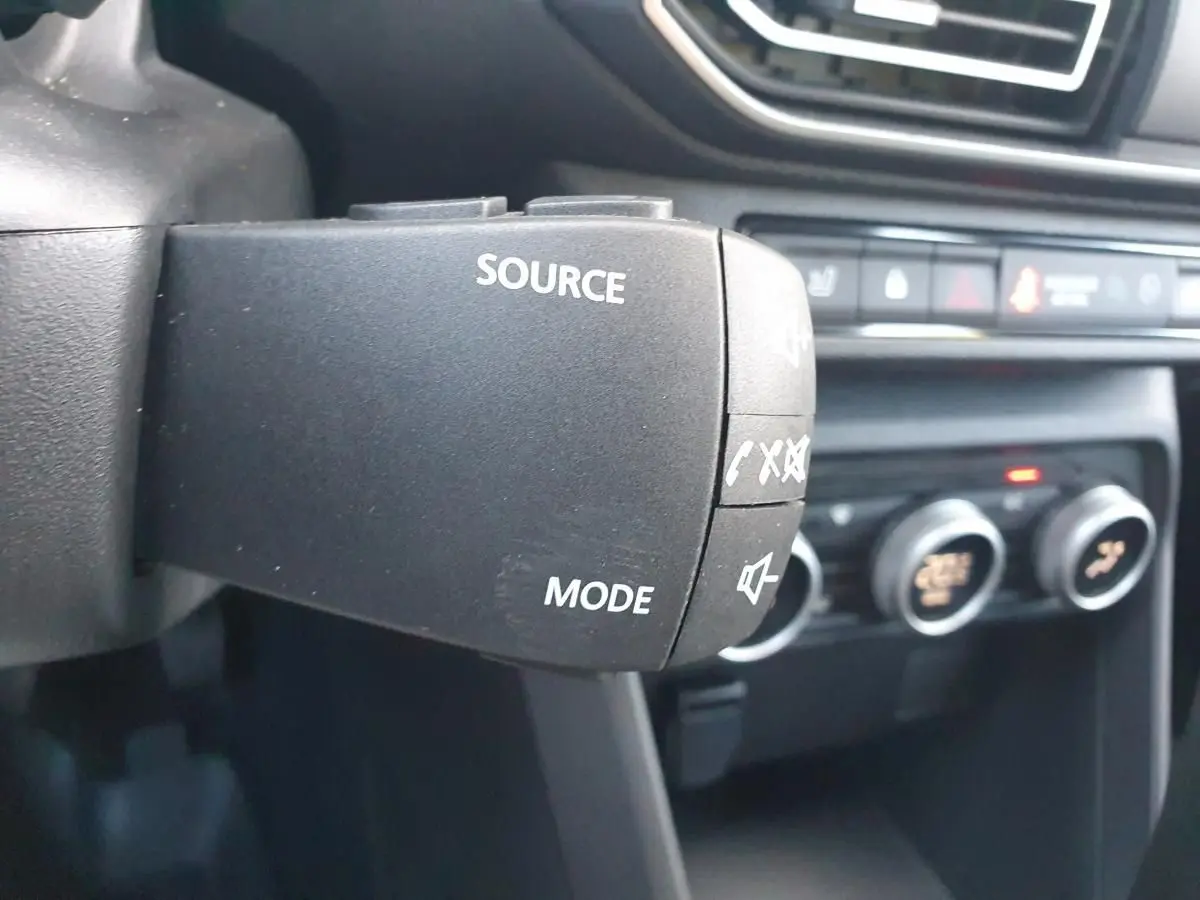 Gros plan sur la commande au volant du DACIA Sandero 2024, mettant en valeur les boutons source et mode audio.
