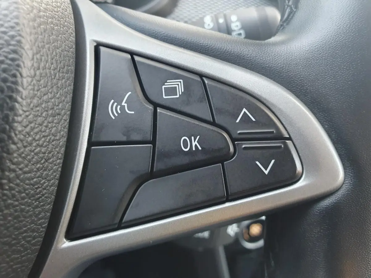 Gros plan sur les commandes multifonctions noires du volant gris d’une Dacia Sandero 2024, boutons OK et flèches visibles.