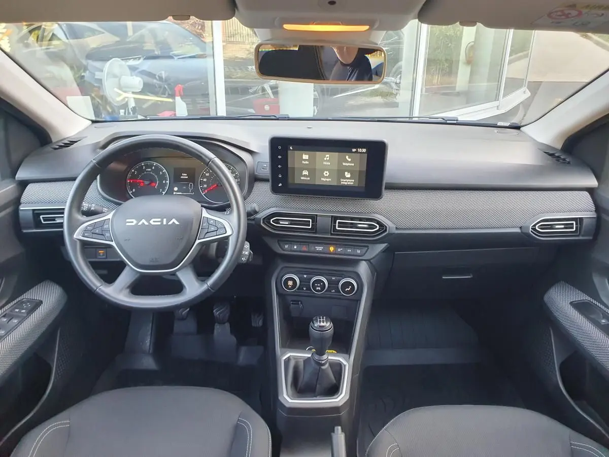 Vue intérieure avant du tableau de bord et volant DACIA Sandero 2024 avec écran tactile et boîte manuelle.