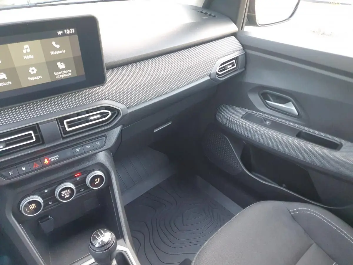 Intérieur de la Dacia Sandero 2024 côté passager, tableau de bord gris avec écran tactile et climatisation automatique.
