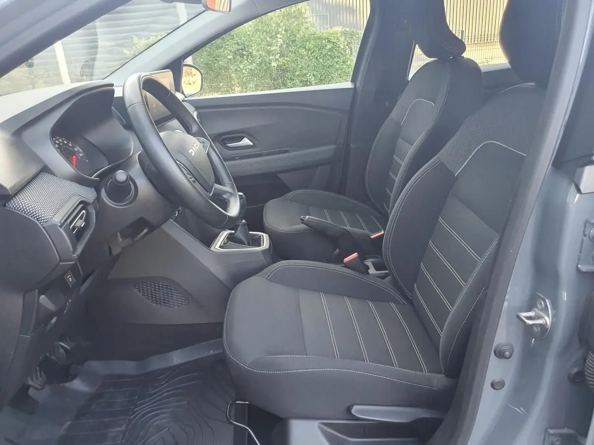 Vue intérieure côté conducteur de la Dacia Sandero gris urbain 2024 avec sièges avant chauffants et volant réglable.