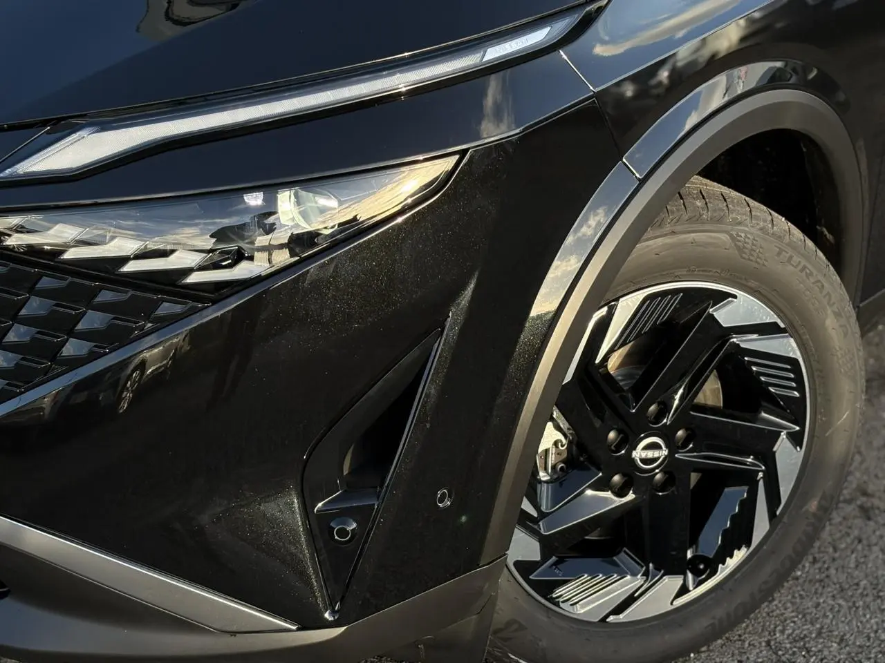 Gros plan sur l'avant droit noir Kuro du Nissan Qashqai III e-Power, mettant en valeur le phare LED et la jante alliage 18 pouces.