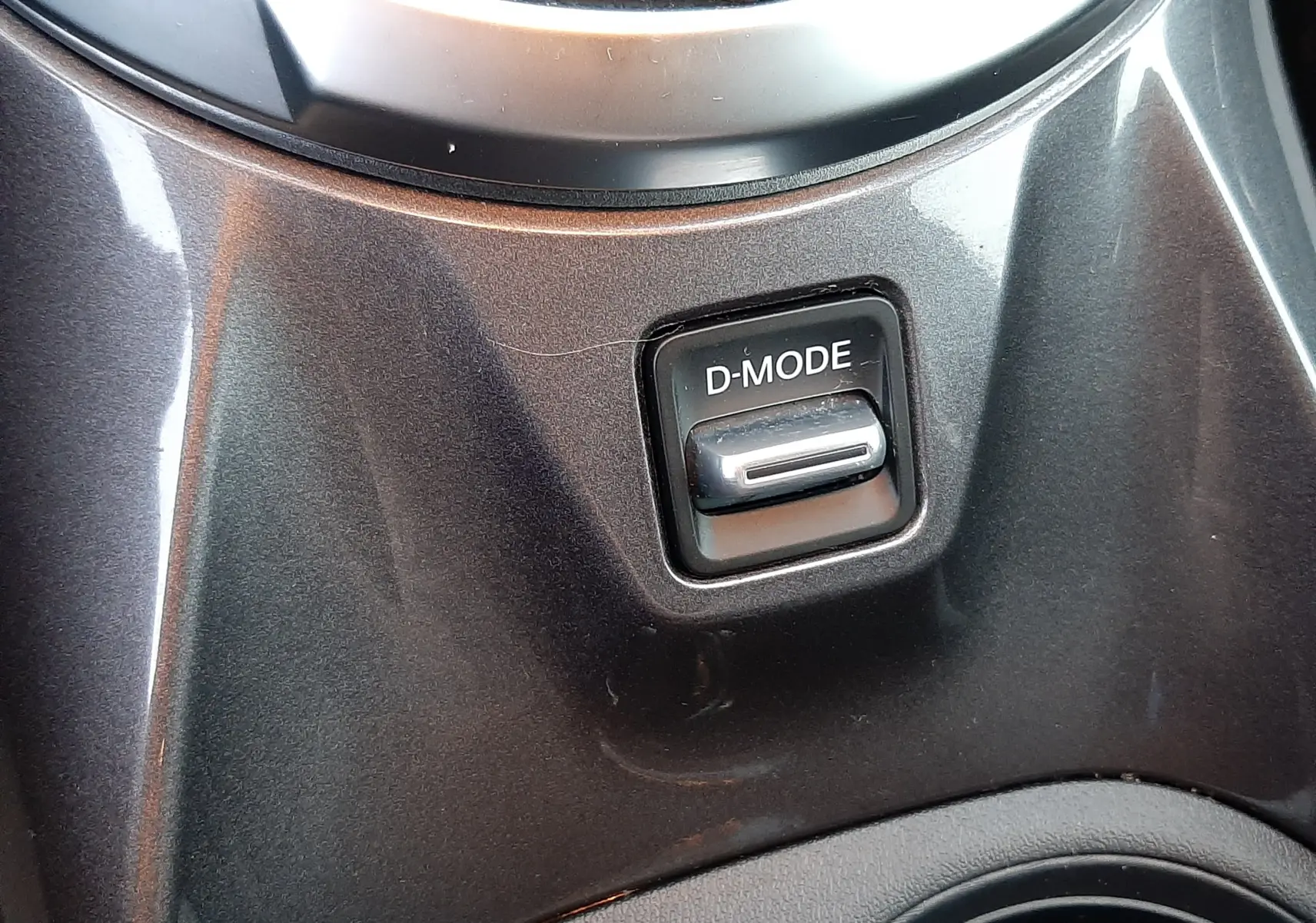 Gros plan sur le bouton D-MODE près du levier de vitesses dans l'habitacle gris perle métal du Nissan Juke 2024.