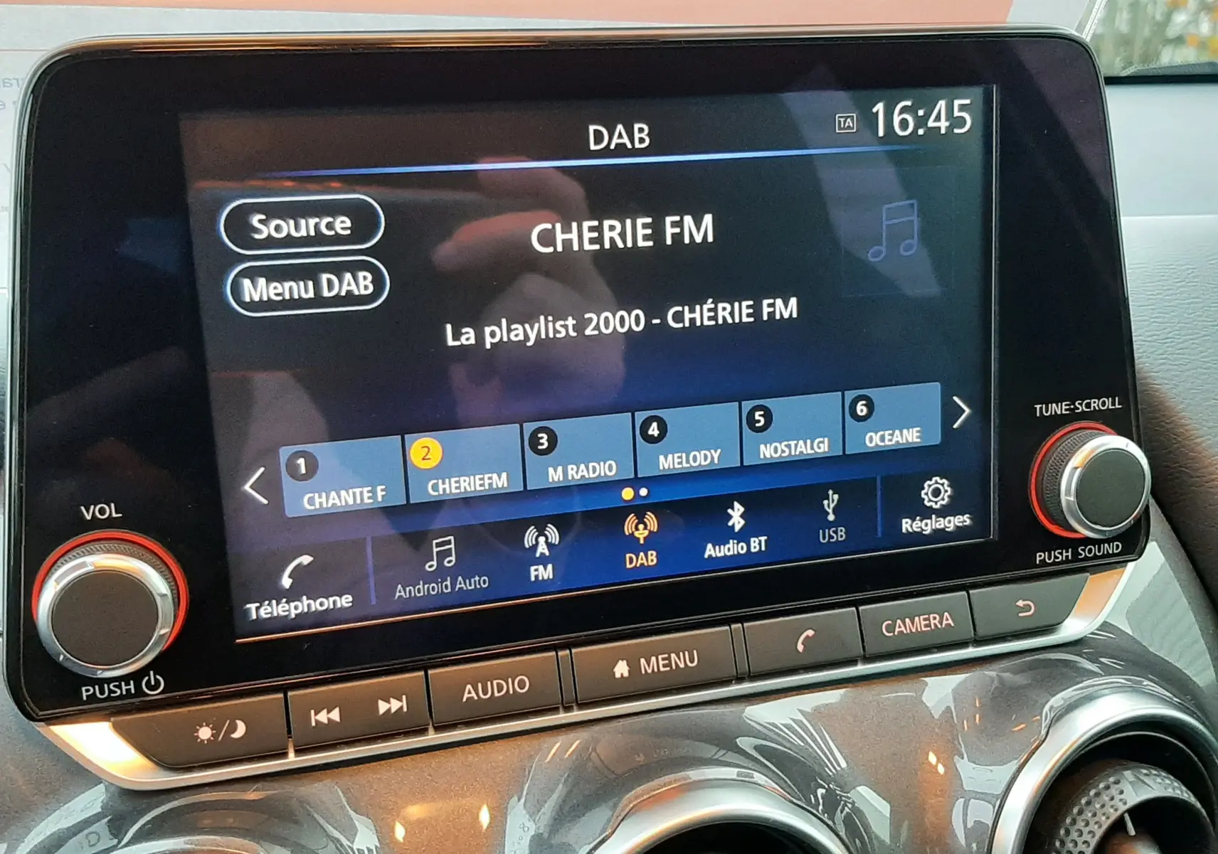 Écran tactile central du Nissan Juke 2024 gris perle, affichant la radio DAB sur CHERIE FM avec commandes autour.
