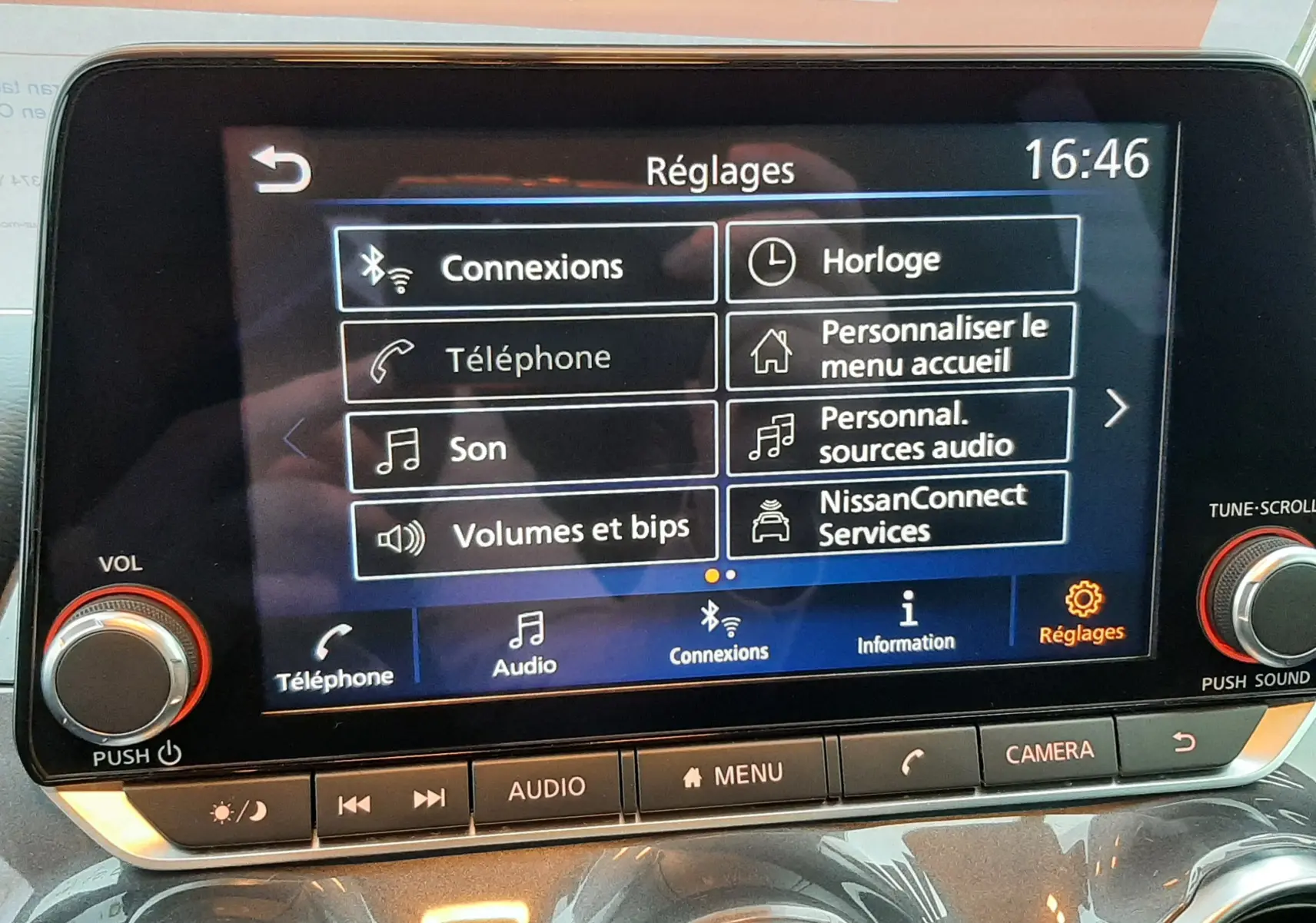 Écran tactile central du Nissan Juke 2024 gris perle, affichant le menu Réglages avec options de connexion et audio.