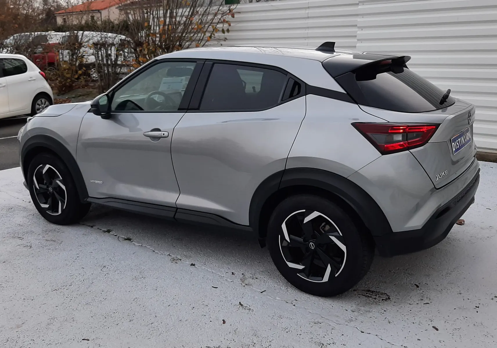 Nissan Juke gris perle métal vu de trois quarts arrière droit, avec jantes noires et toit noir contrasté.