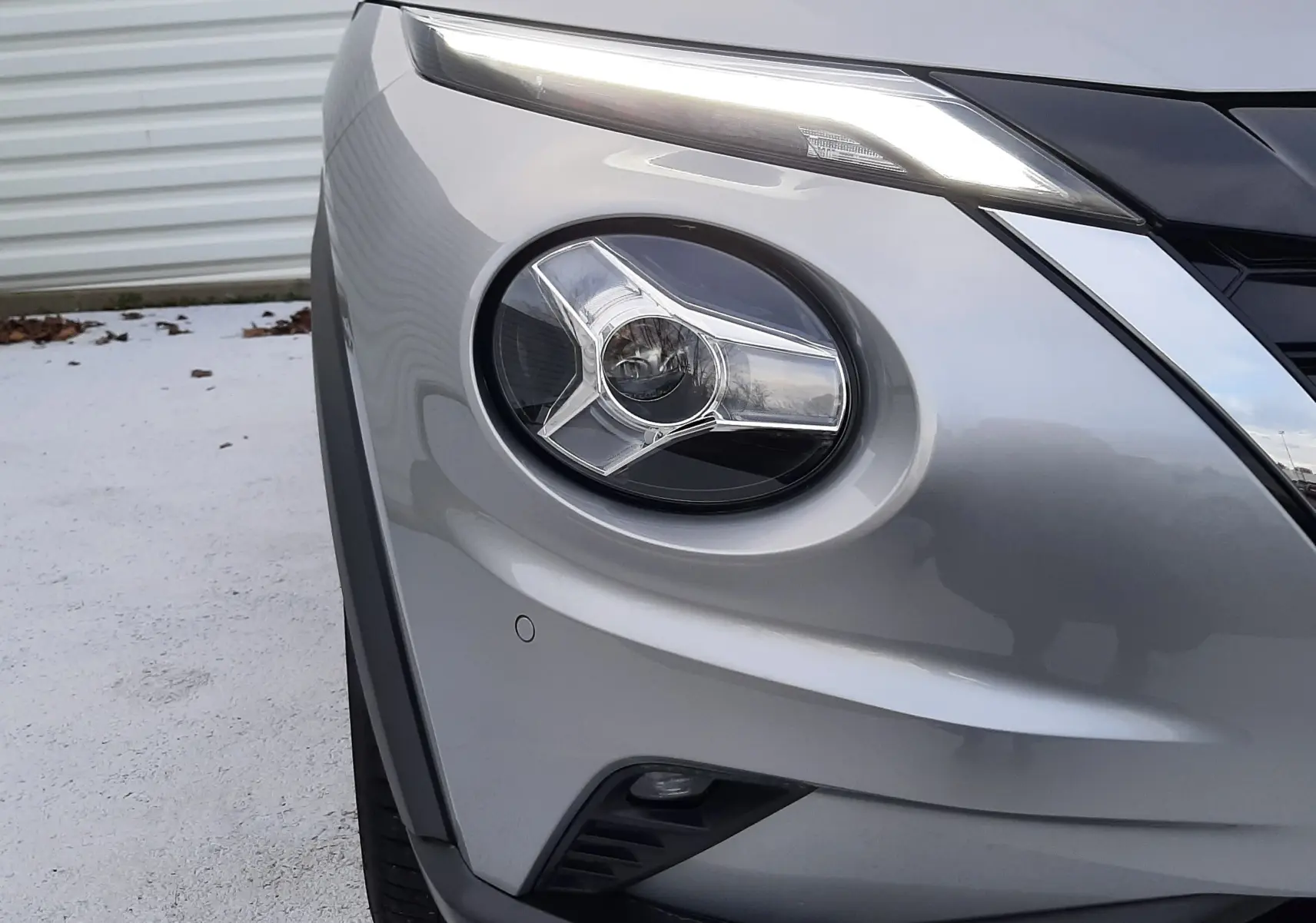 Gros plan sur l'avant droit du Nissan Juke gris perle métal 2024, mettant en valeur son phare rond et son feu LED fin supérieur.