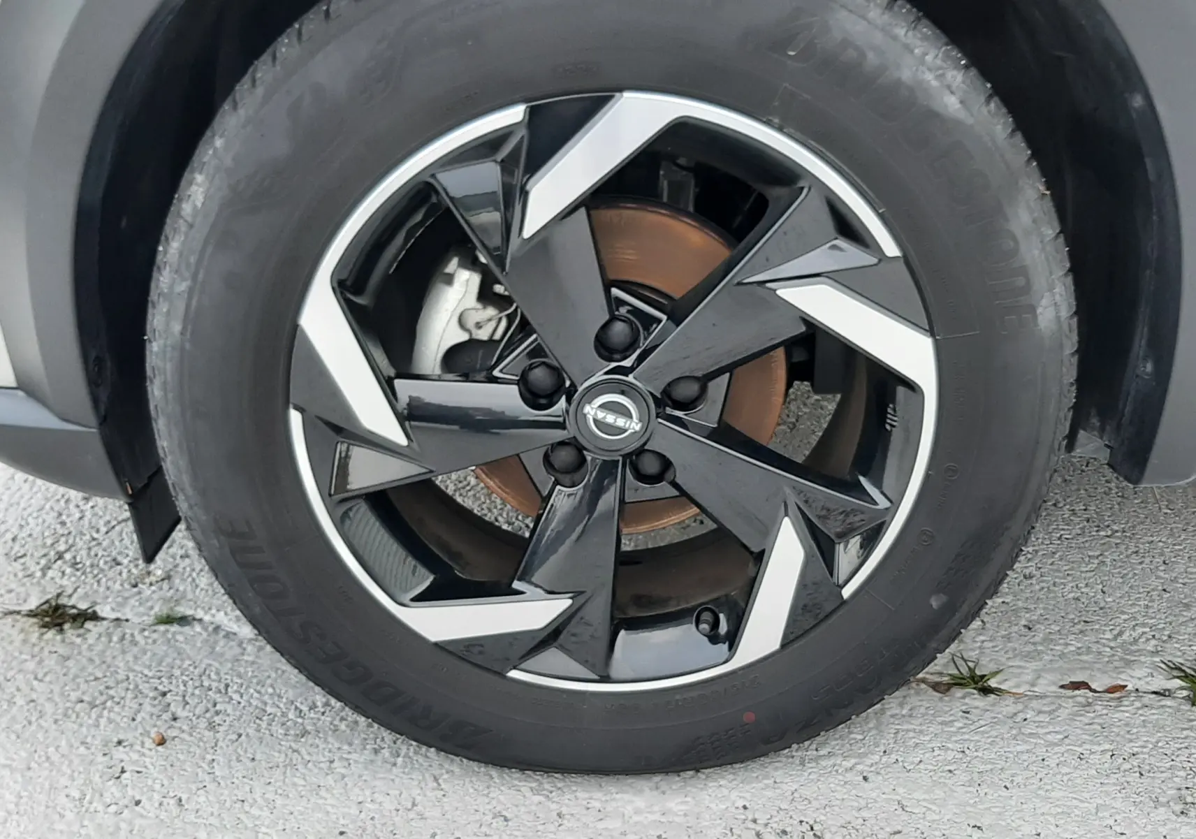 Gros plan sur la roue avant droite d'un Nissan Juke gris perle métal avec jante noire et argentée au design anguleux.