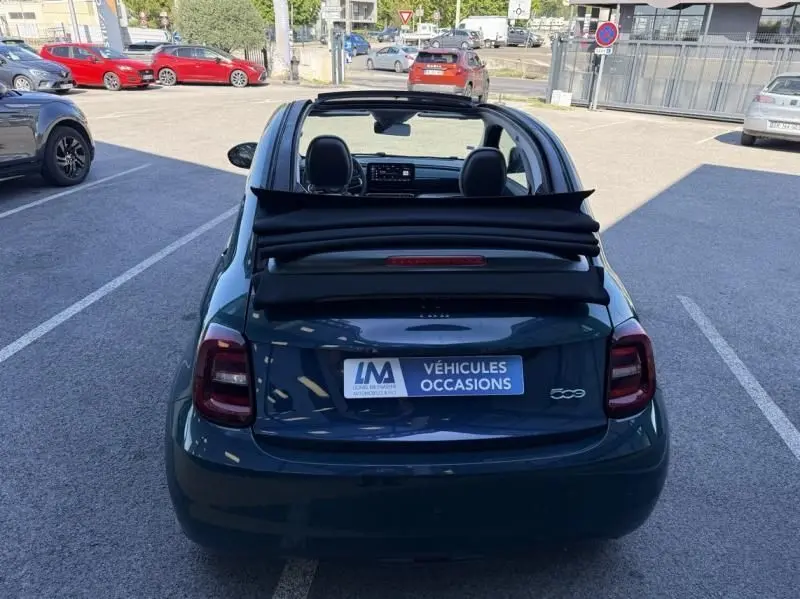 Vue arrière d'une FIAT 500C 118 cv icone électrique 2021 en vert foncé métal avec toit ouvrant replié, stationnée en extérieur.