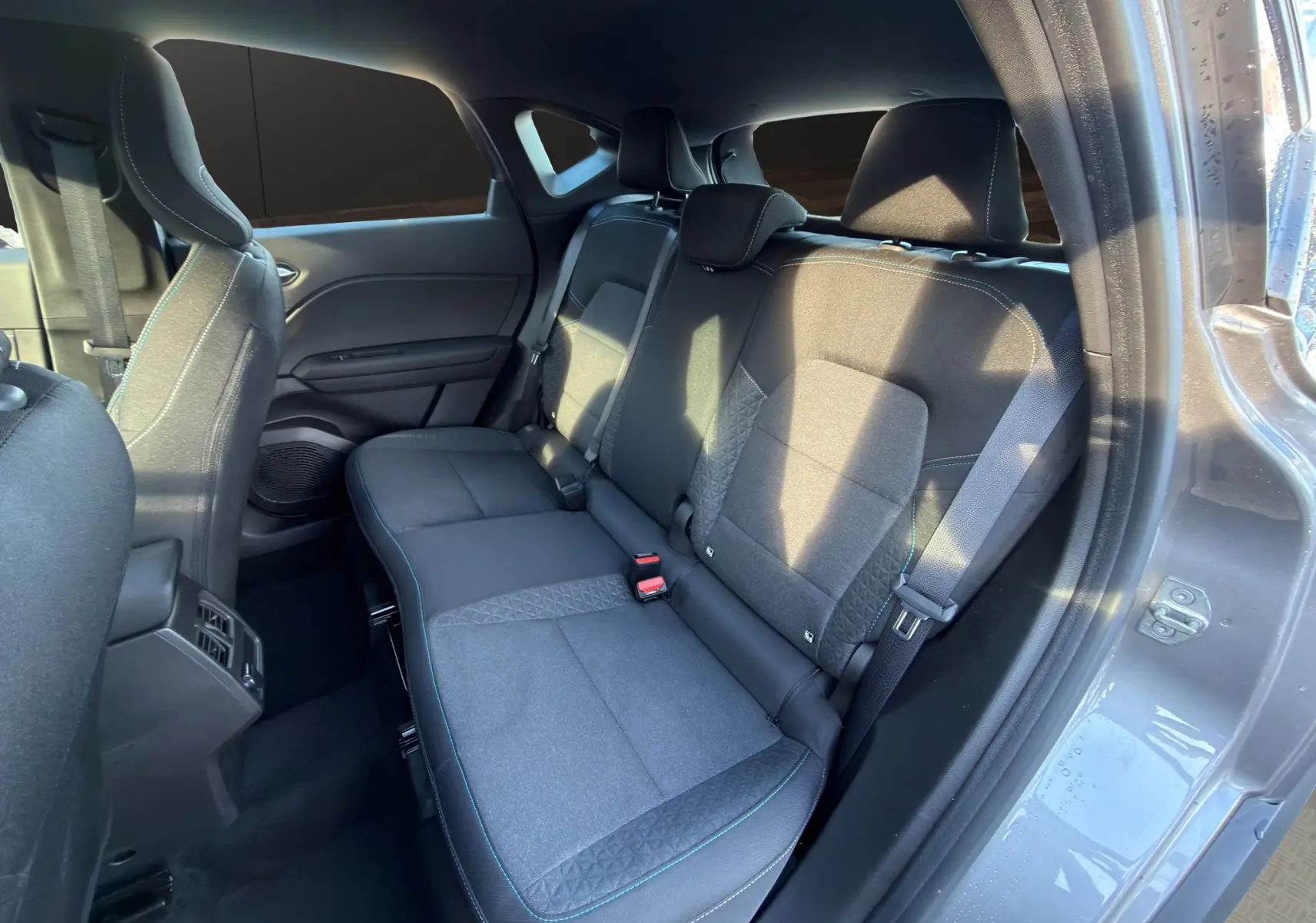 Vue intérieure arrière côté droit du Renault Captur 2024 gris Cassiopée, montrant les sièges arrière en tissu avec surpiqûres bleues.