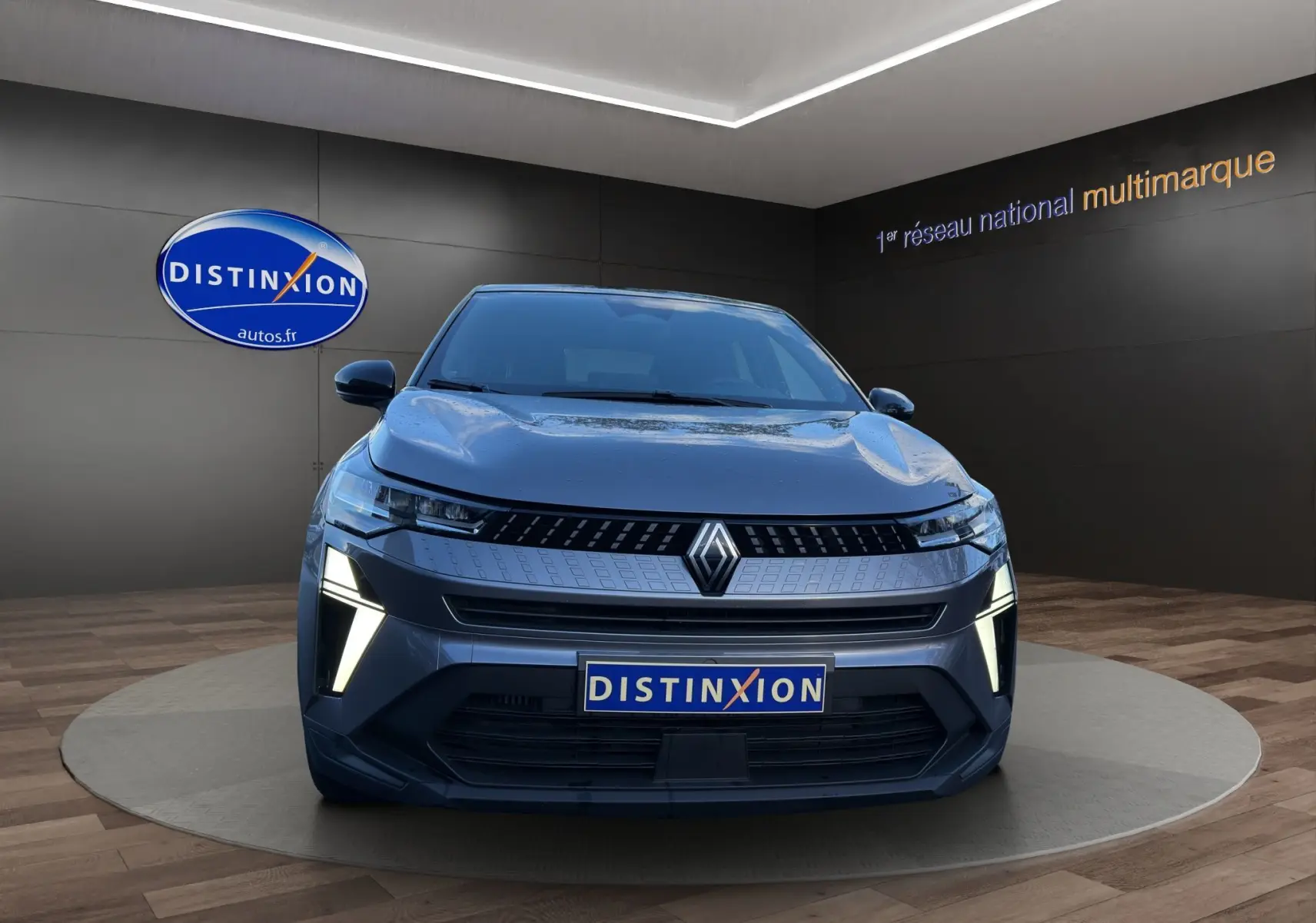 Vue de face du Renault Captur 2024 gris Cassiopée avec toit noir, feux LED allumés et calandre distinctive.