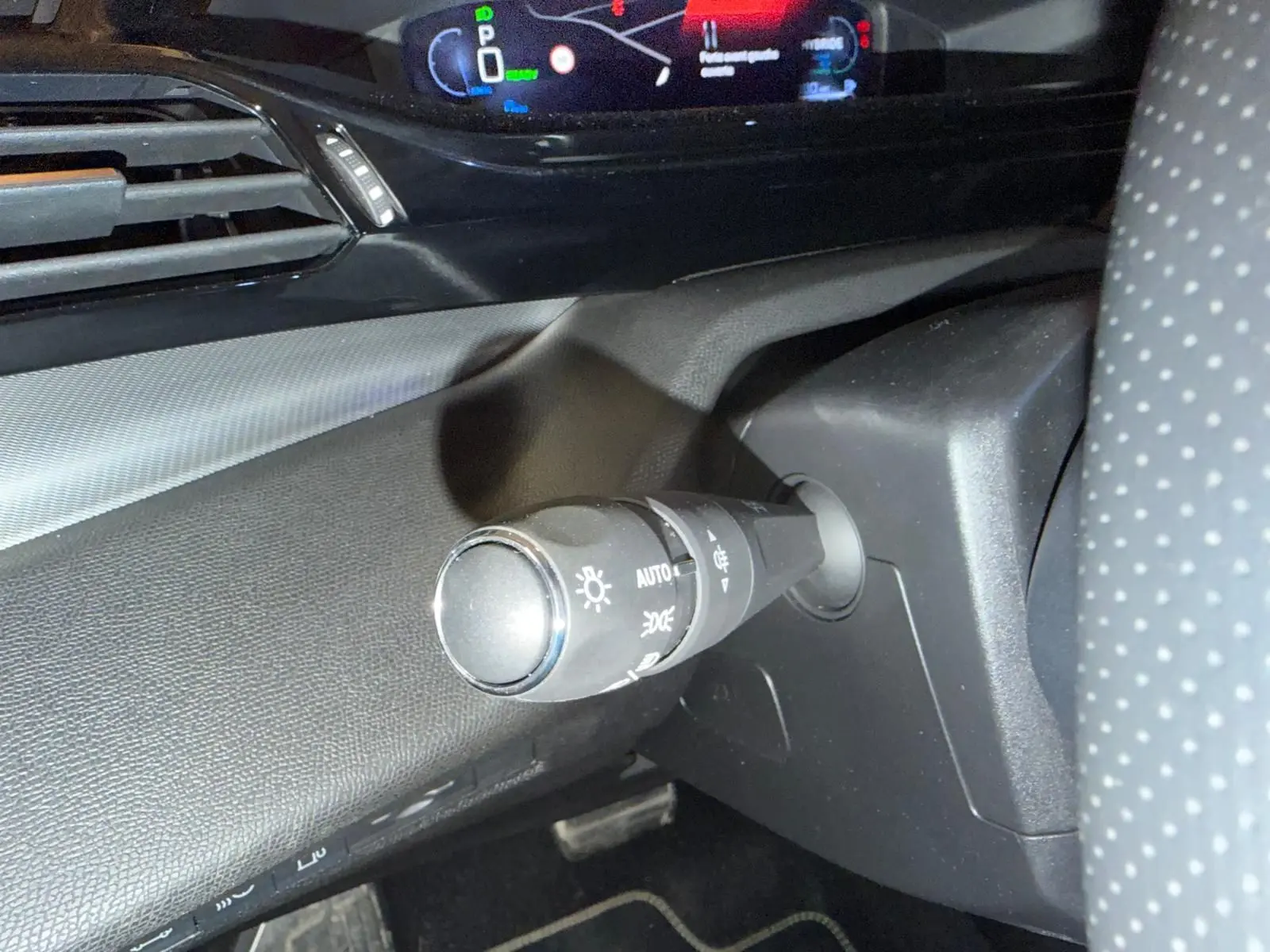 Gros plan sur la commande des feux à gauche du volant perforé dans l’habitacle sombre du Peugeot 408 gris.