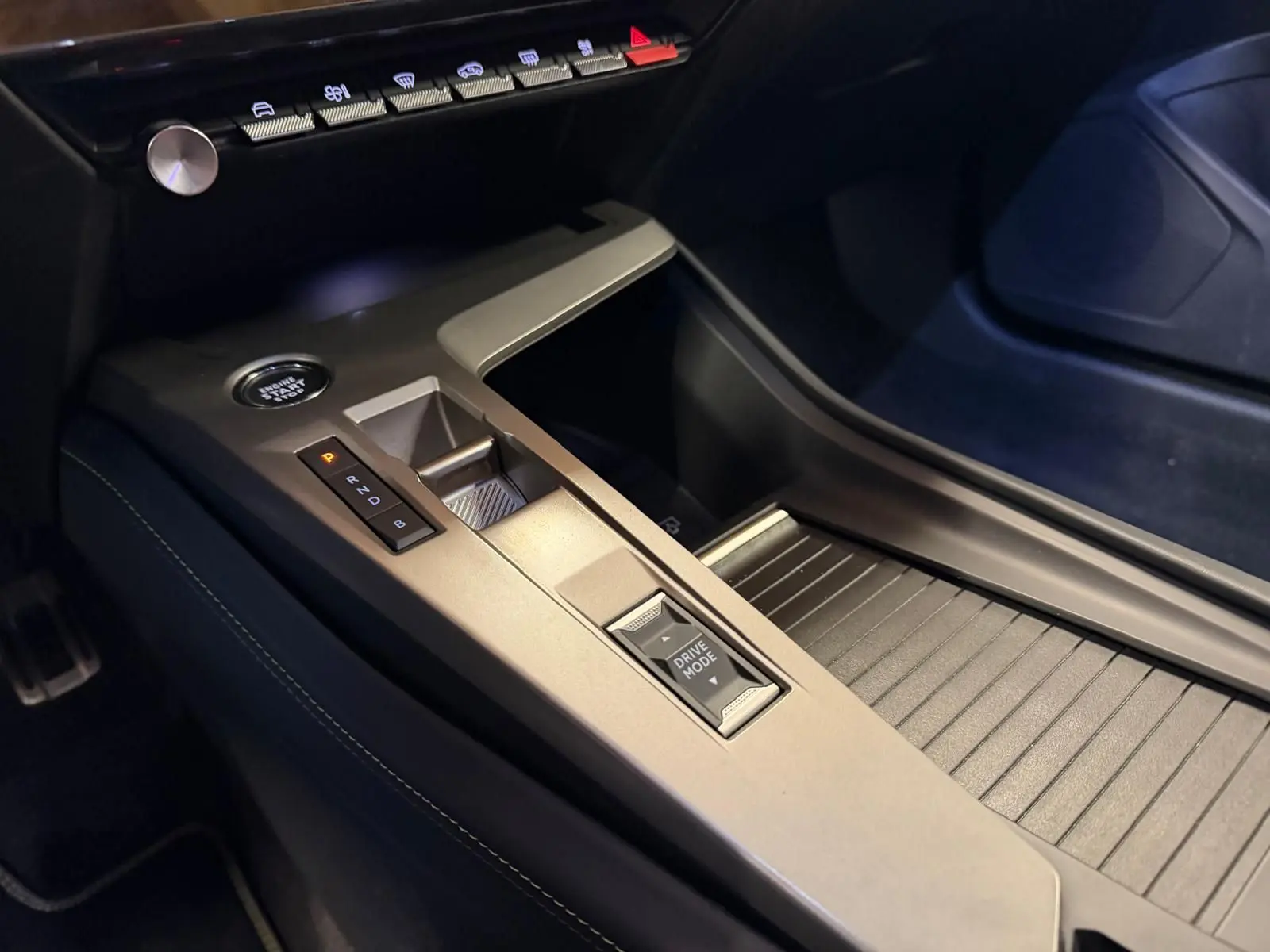 Gros plan sur la console centrale grise de la Peugeot 408 2025 avec bouton Drive Mode et démarrage sans clé.