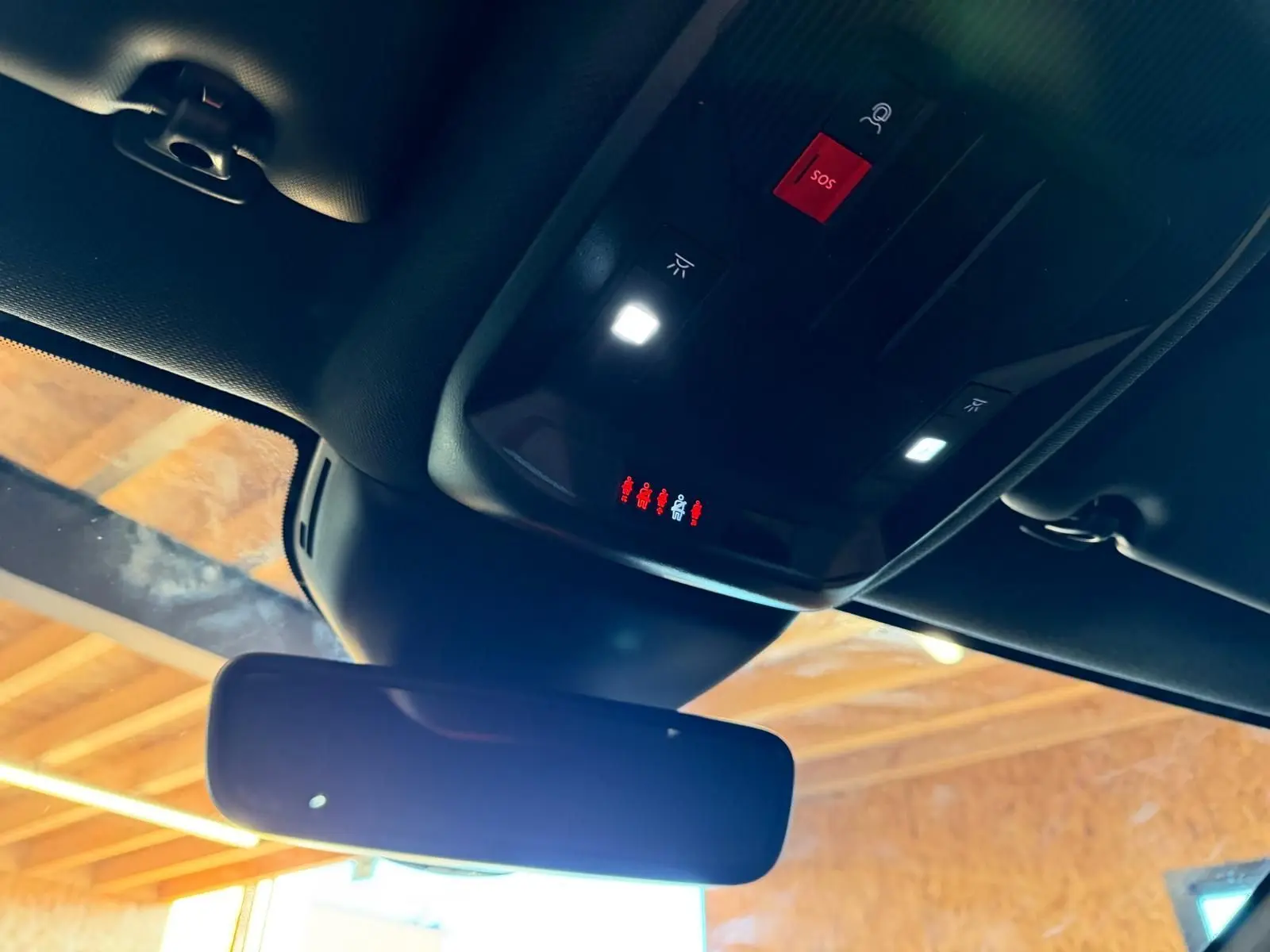 Vue intérieure du plafond noir Mistral avec rétroviseur et commandes d'éclairage et bouton SOS rouge du Peugeot 408 gris hybride rechargeable.