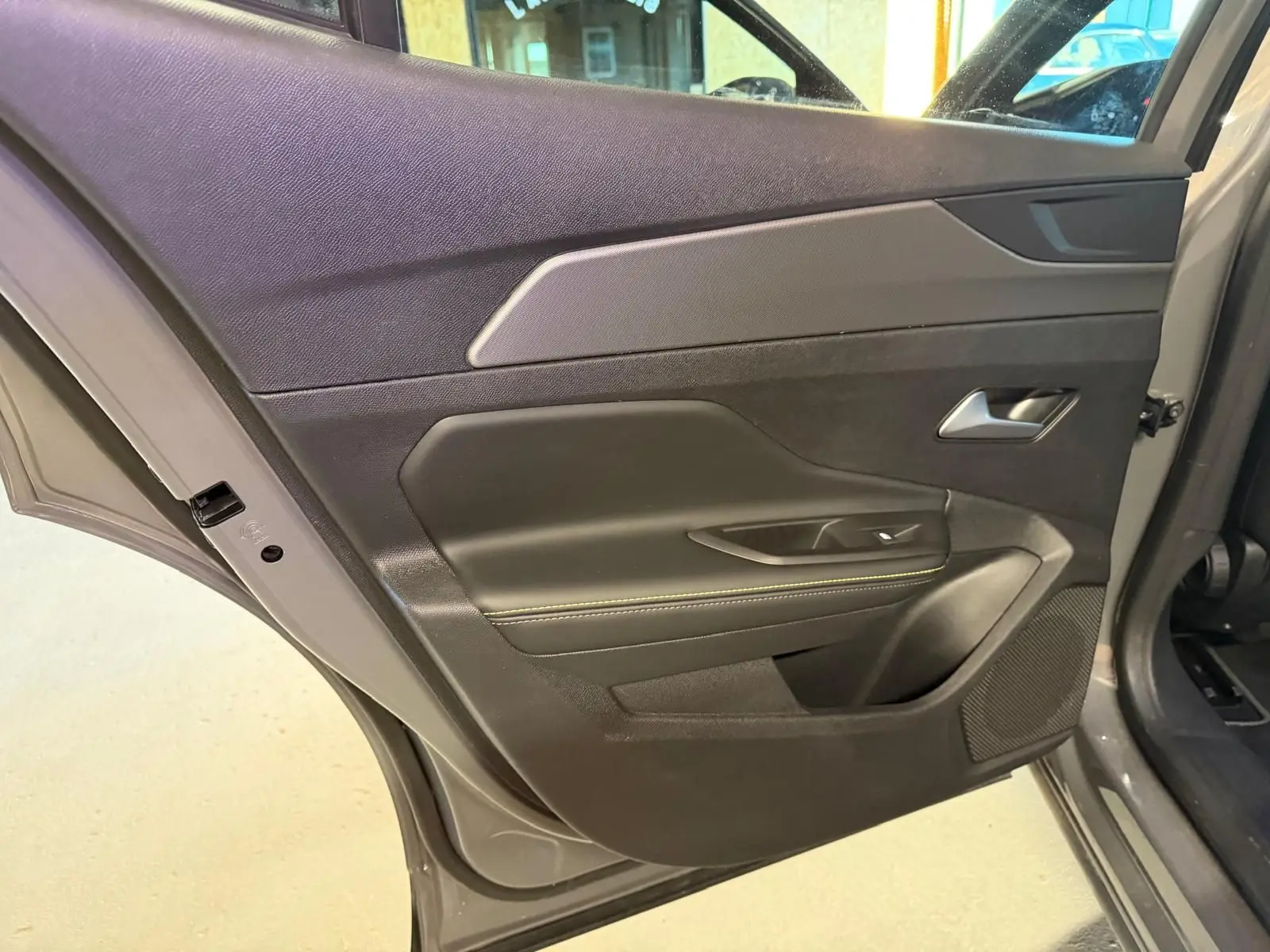 Vue rapprochée de la porte arrière gauche gris Selenium de la Peugeot 408 2025 avec surpiqûre verte et poignée alu.