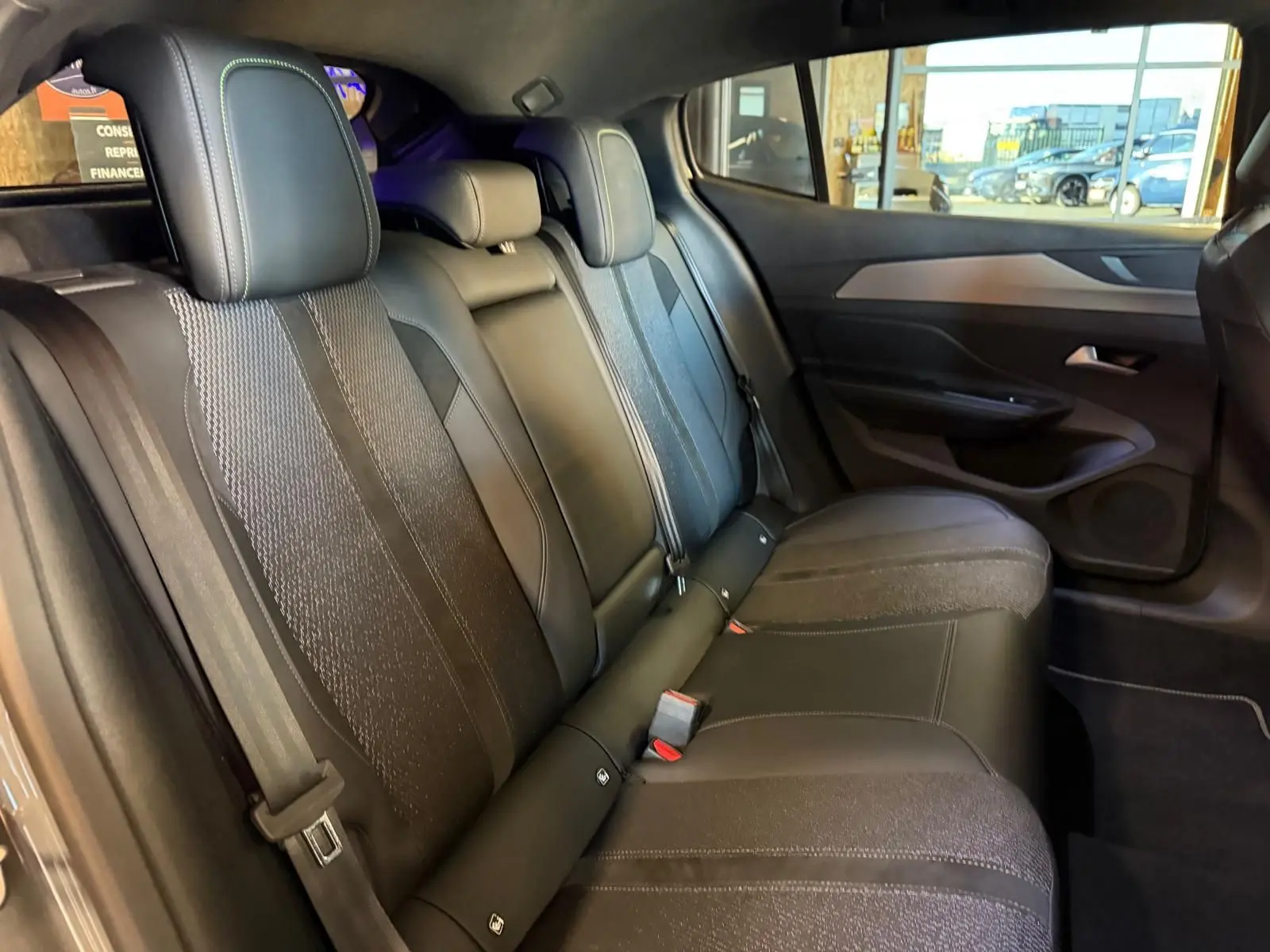 Vue intérieure des sièges arrière noirs avec surpiqûres vertes et panneaux de porte gris sur Peugeot 408 2025.