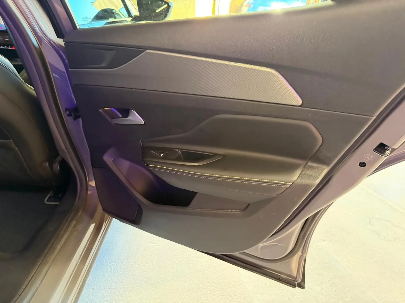 Vue rapprochée de la porte arrière gauche grise du Peugeot 408 2025 avec surpiqûres vertes et poignée argentée.