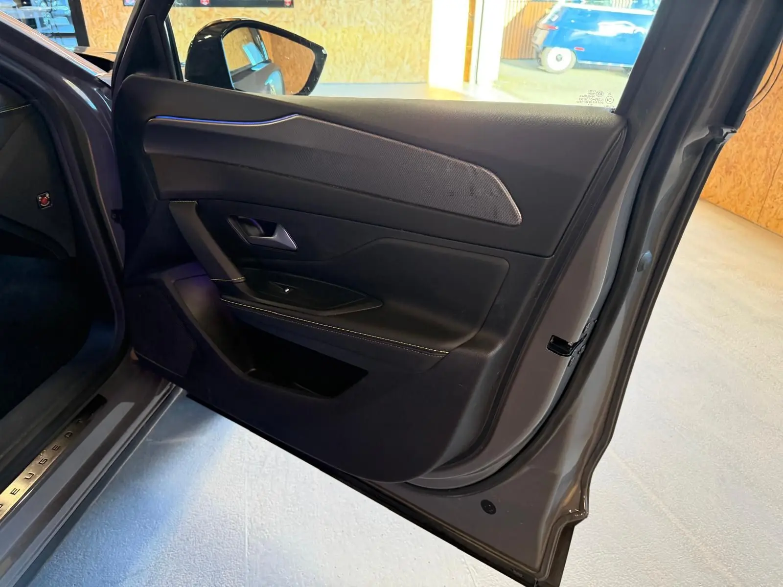 Vue intérieure côté gauche de la porte arrière grise du Peugeot 408 2025 avec surpiqûres vertes et éclairage d'ambiance bleu.