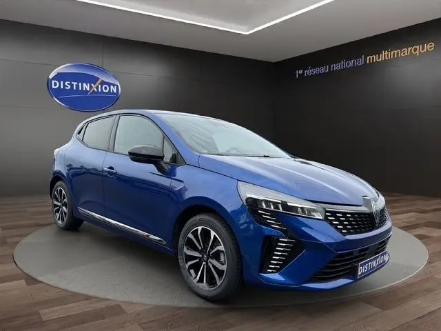 Vue 3/4 avant d'une Renault Clio Techno E-Tech hybride 2025 bleu avec détails chromés et phares LED distinctifs.