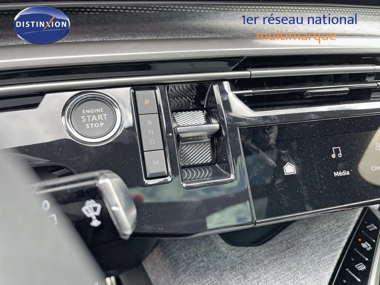 Gros plan sur la console centrale noire brillante du Peugeot 5008 Hybrid 2025 avec bouton start/stop et commandes de boîte automatique.