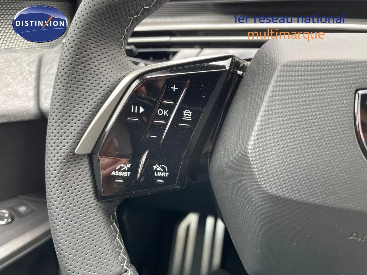 Gros plan sur les commandes au volant du Peugeot 5008 Hybrid 136ch GT, volant cuir perforé noir.
