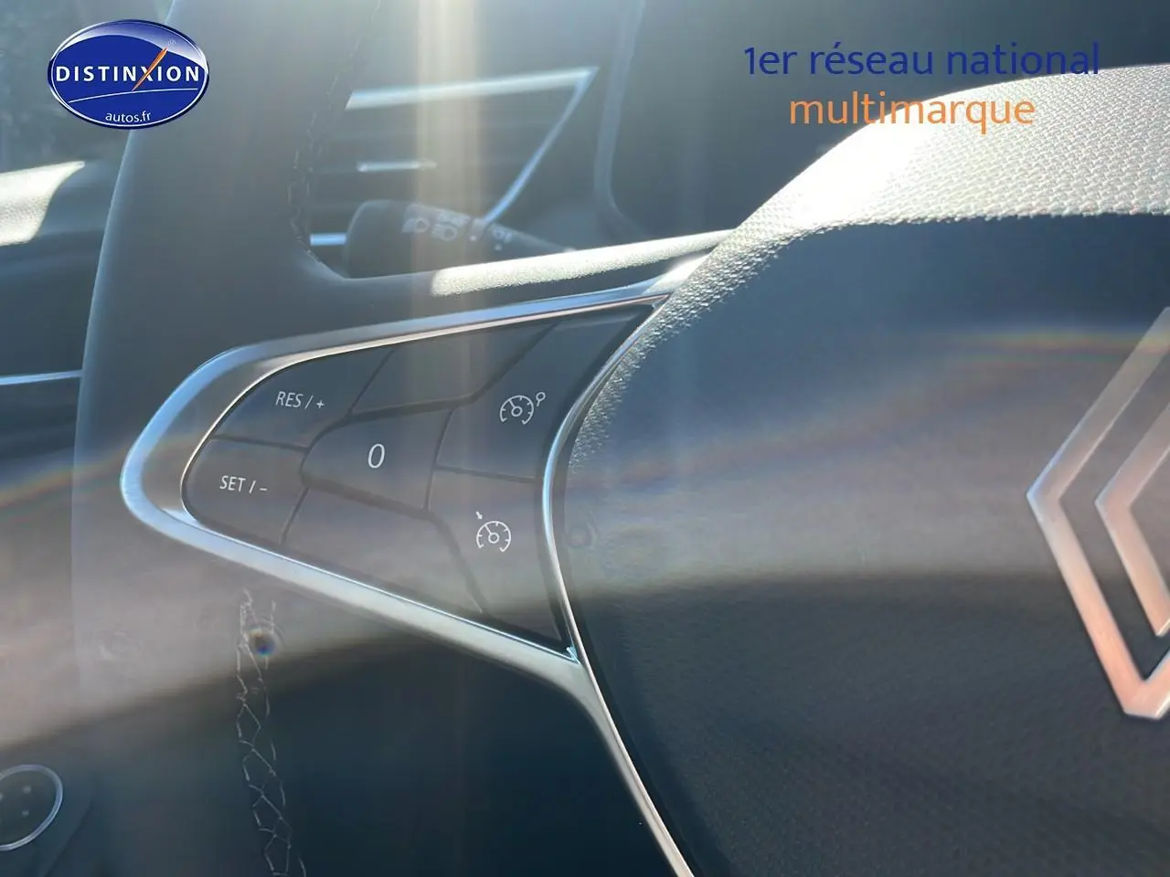 Gros plan sur les commandes du régulateur de vitesse au volant de la Renault Clio V Diesel bleu iron, intérieur lumineux.