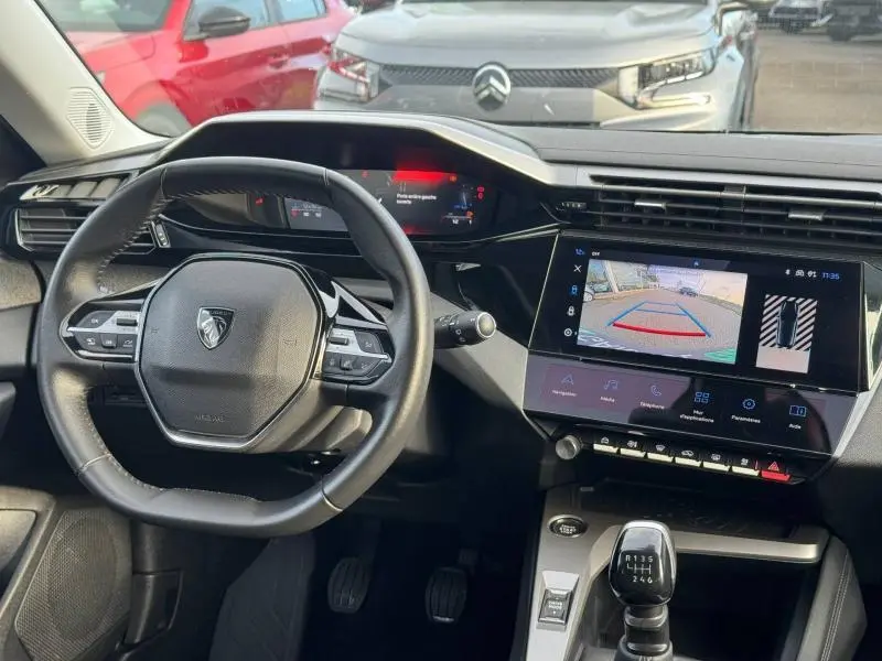 Vue intérieure du poste de conduite de la Peugeot 308 2024, volant multifonction et écran tactile avec caméra de recul affichée.