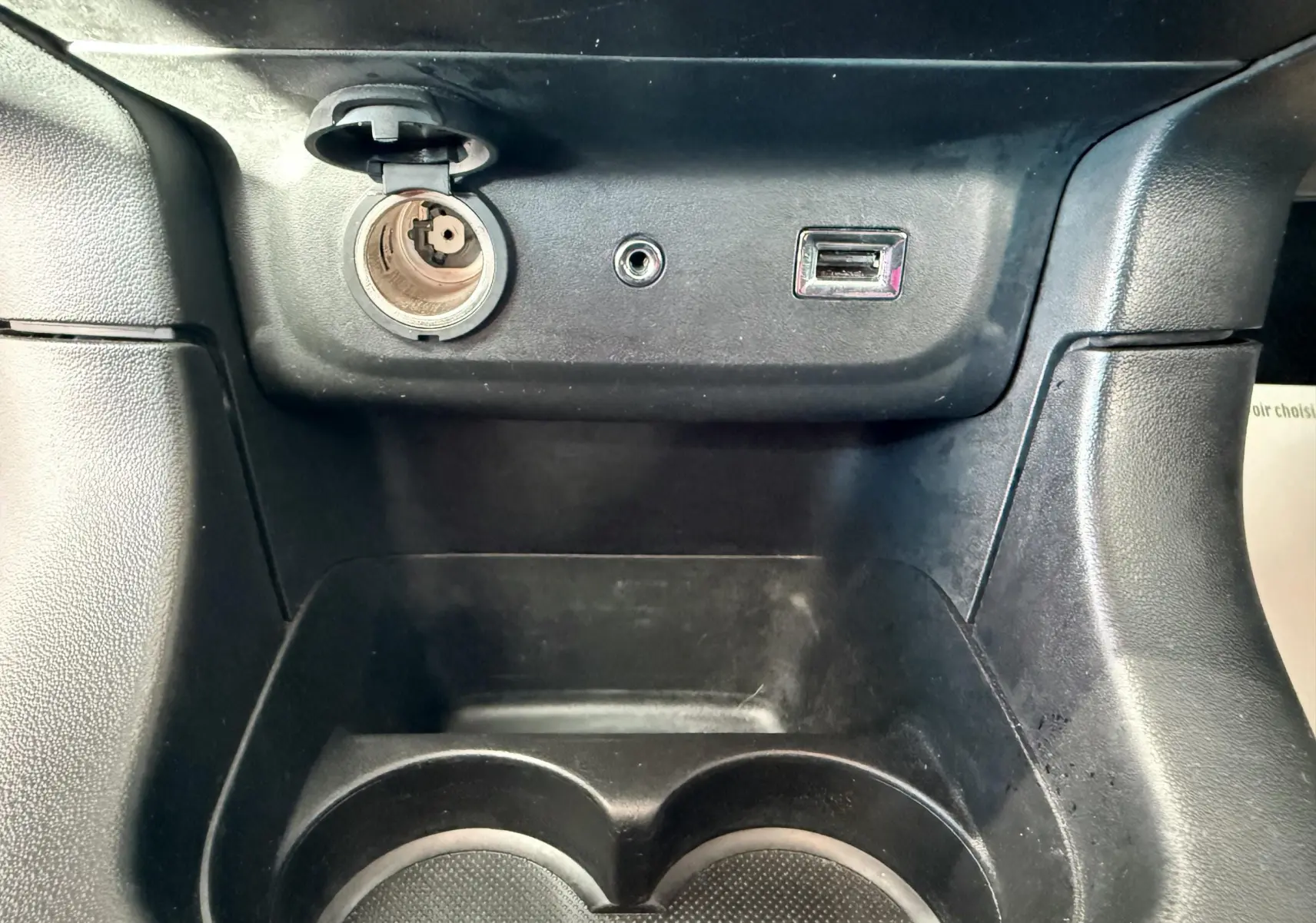 Vue rapprochée de la console centrale noire avec prise allume-cigare, port USB et prise auxiliaire sur Citroën C3 blanche.