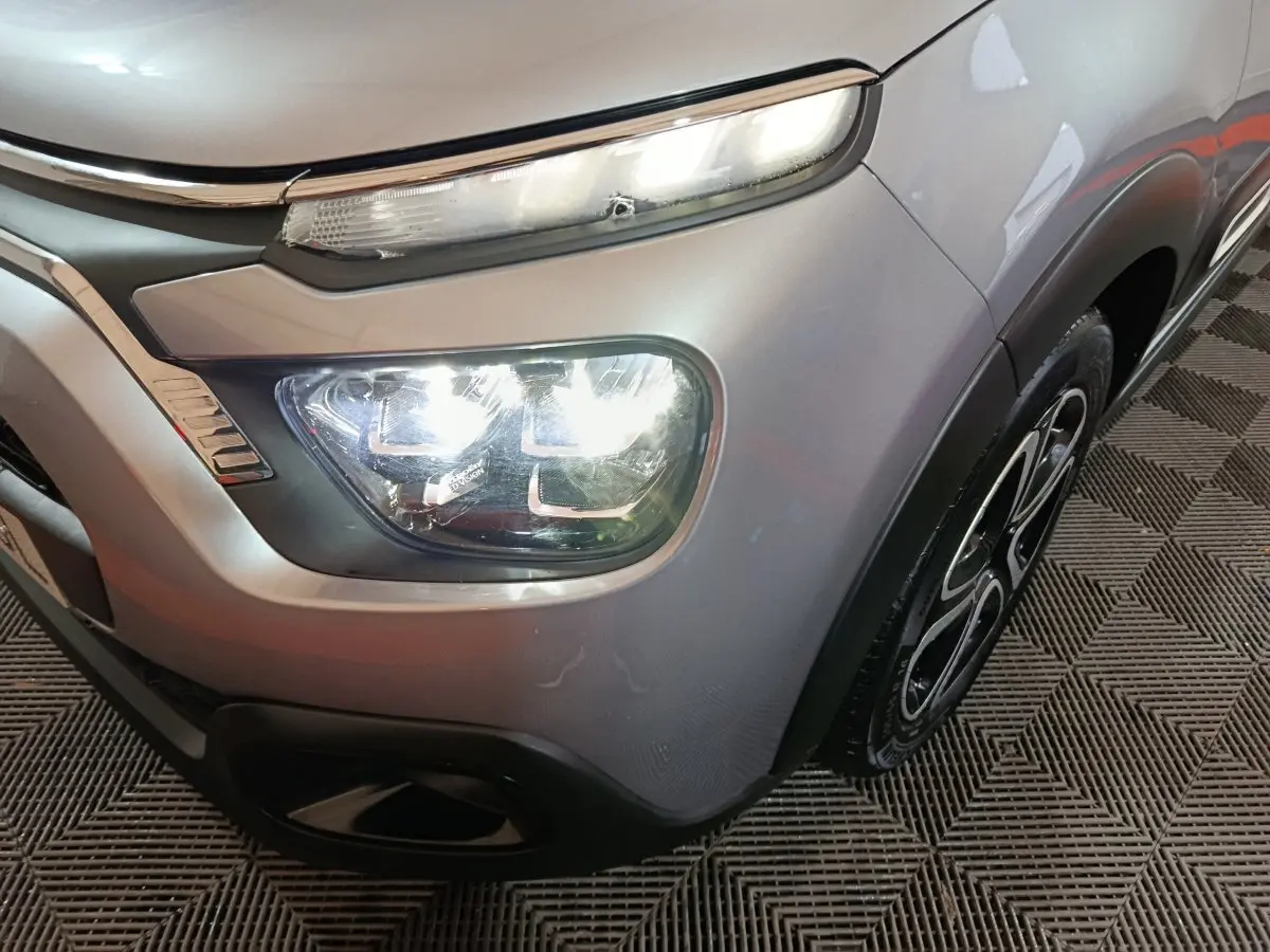 Gros plan sur l'avant droit gris clair de la Citroën C3 2024, mettant en valeur les phares LED et la roue au design distinctif.