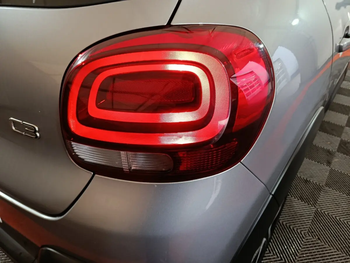 Gros plan sur le feu arrière droit rouge d'une Citroën C3 gris clair, avec logo C3 visible sur la carrosserie.